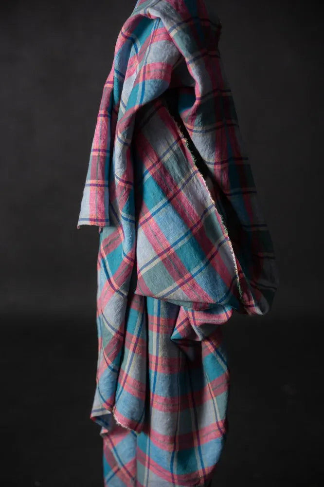 Plaid fabric with pink and blue patterns draped over a dark background